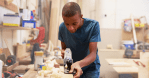 Young boy using a hand planer on a piece of wood in a carpentry workshop, focusing intently on his work.