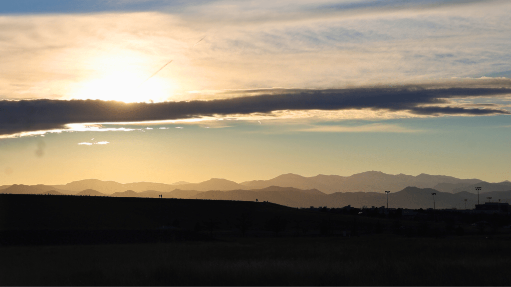A wide landscape at sunset with layered mountain silhouettes in the distance and a glowing sky, symbolizing reflection, patience, and long-term growth during quiet seasons.