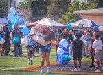 Family members, community supporters, and children gather on the football field holding blue and white balloons during a memorial ceremony honoring 16-year-old De'Quan at the Change for De'Quan Flag Football Game in Denver, Colorado.