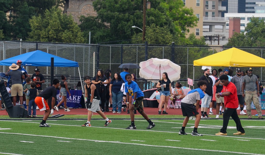 Youth football players line up before a play while families, vendors, and community members watch from the sidelines during the Change for De'Quan event.