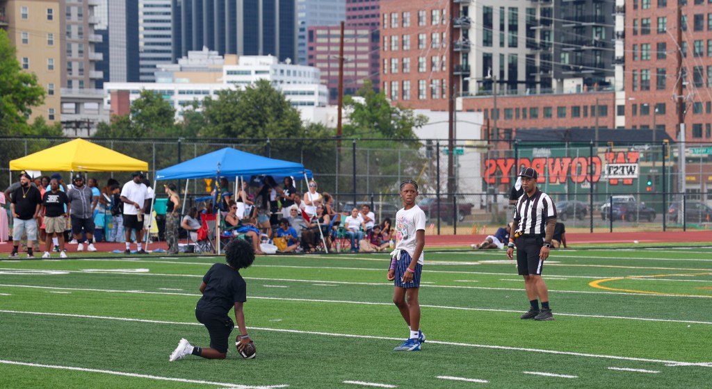 Two youth football players prepare for the next play while a referee watches during the Change for De'Quan flag football event in Denver.