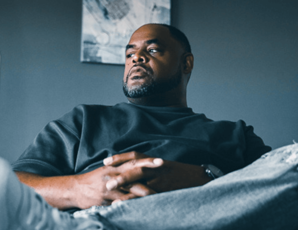 A man sits thoughtfully in a chair, looking out a window in quiet reflection. Featured image for The Resilient Mind essay, "The Mission Keeps Getting Lost," about emotional resilience, leadership, and community.