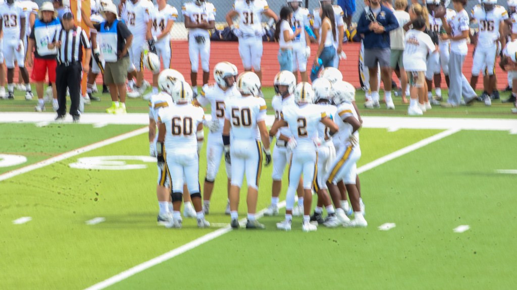 Northfield football players in white uniforms gather in an offensive huddle during the game against Montbello.