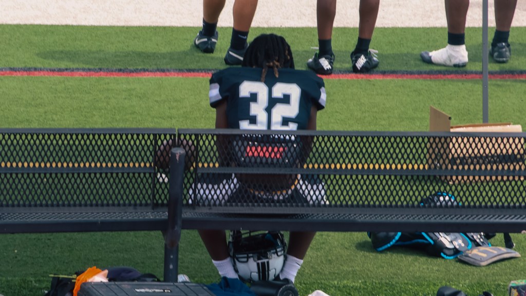 Montbello football player number 32 sits alone on the sideline bench during the game.