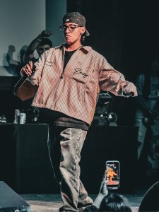 Denver independent artist performing onstage with a microphone during a live local music show.