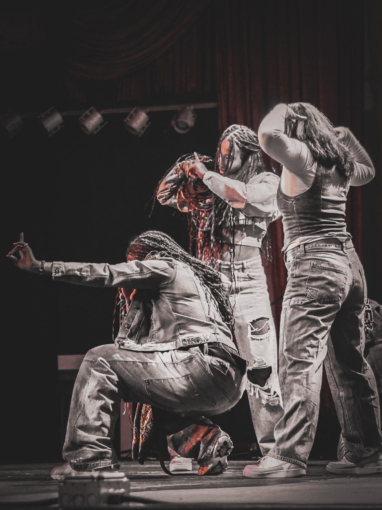 Three female performers sharing the stage during a live Denver music performance, captured in a dramatic, selectively colored photograph.