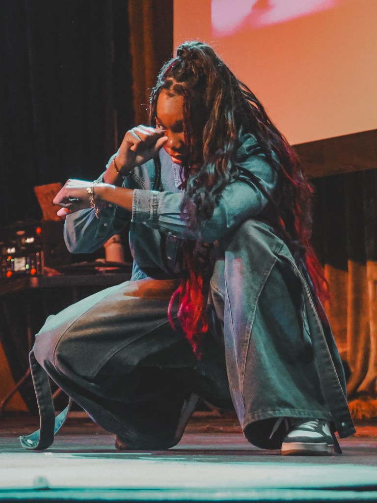 Denver female artist crouched onstage during an expressive moment at a live local music performance.
