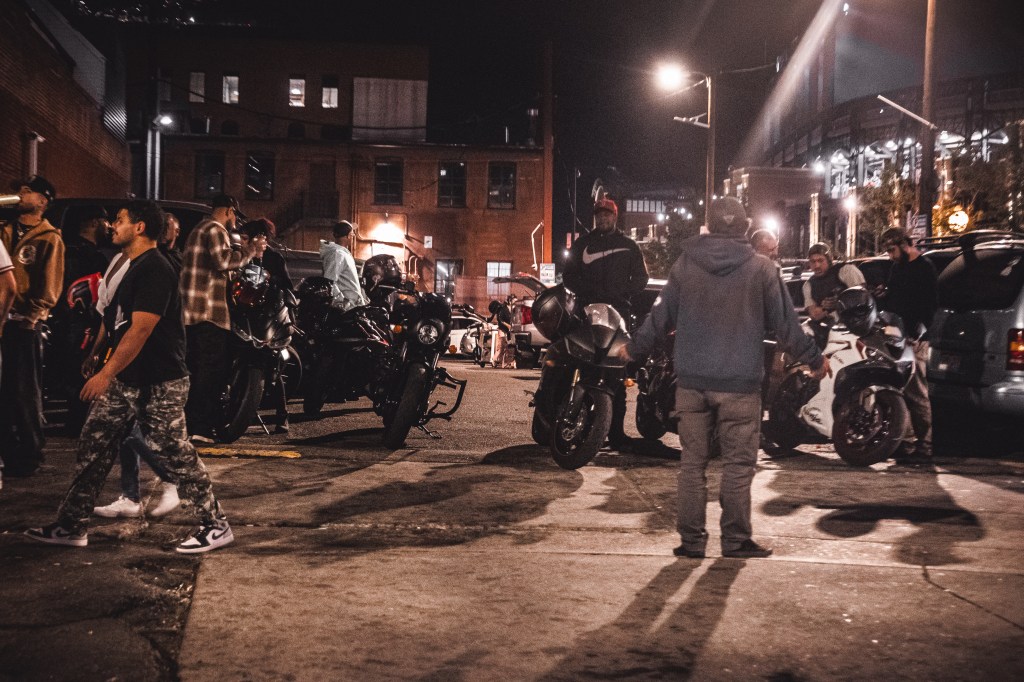 Group of people standing among several parked motorcycles during a nighttime gathering.