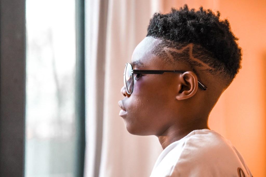 ide-profile portrait of a young boy wearing glasses and looking toward a bright window.