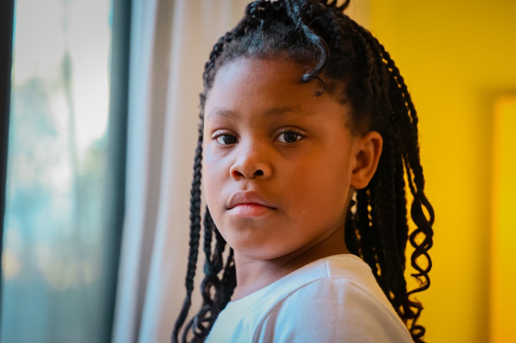 Close-up portrait of a young girl with braided hair looking directly toward the camera.